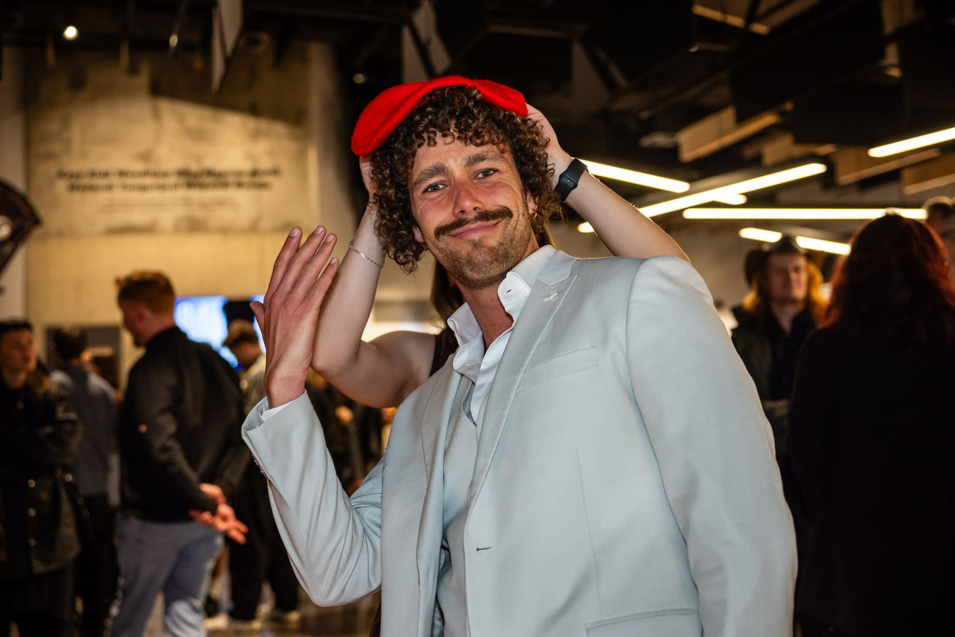 Man In A Crowded Room Smiling At The Camera, Wearing A Red Beret.